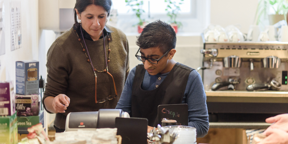 Woman helping young man with learning disabilities learn how to use a cafe till