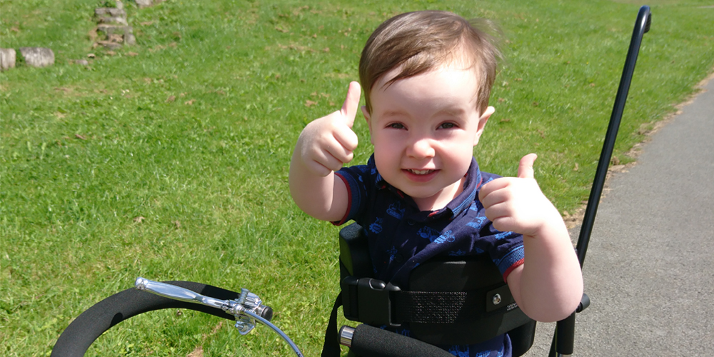 Little boy on adapted trike giving thumbs up