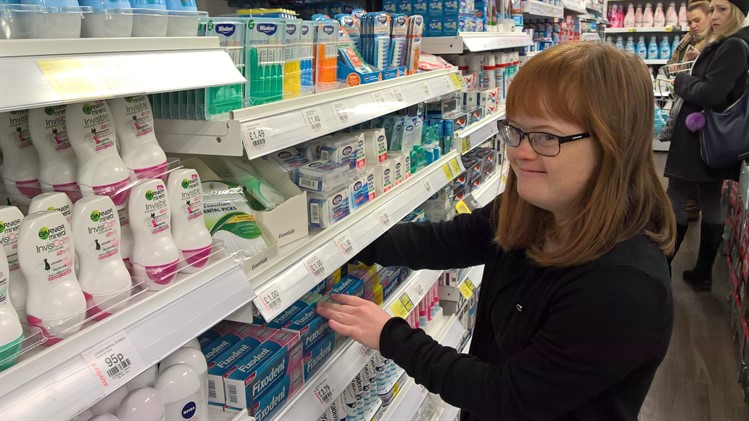 Young woman stacking shelves in a Savers health and beauty shop aisle