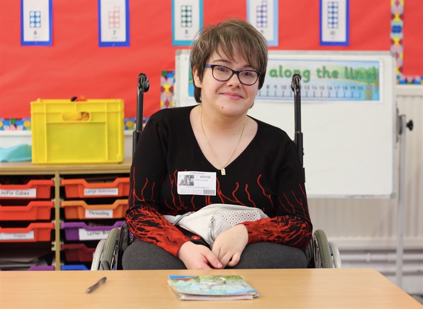 Young smiling woman in a wheelchair, sitting in a primary school classroom and looking at the camera