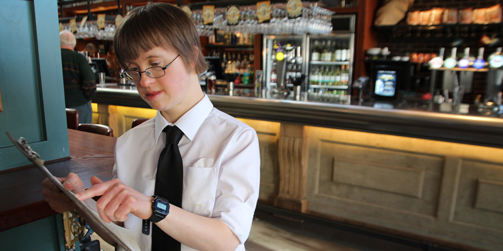 Young woman with learning disabilities working as a waitress holding a clipboard