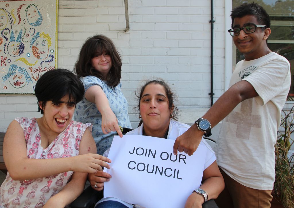 Four young people people with learning disabilities hold adn point to a sign saying "join our council"