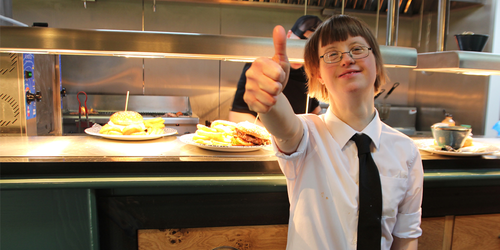 Smiling young woman with learning disabilities working as a waitress giving thumbs up