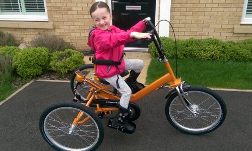 Smiling girl on an orange adapted trike