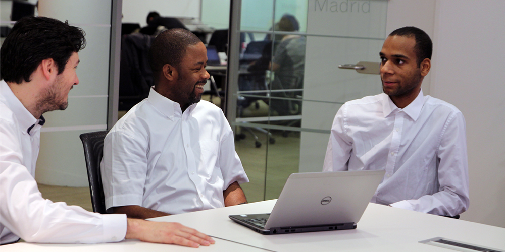 3 young men sitting at a desk with a laptop