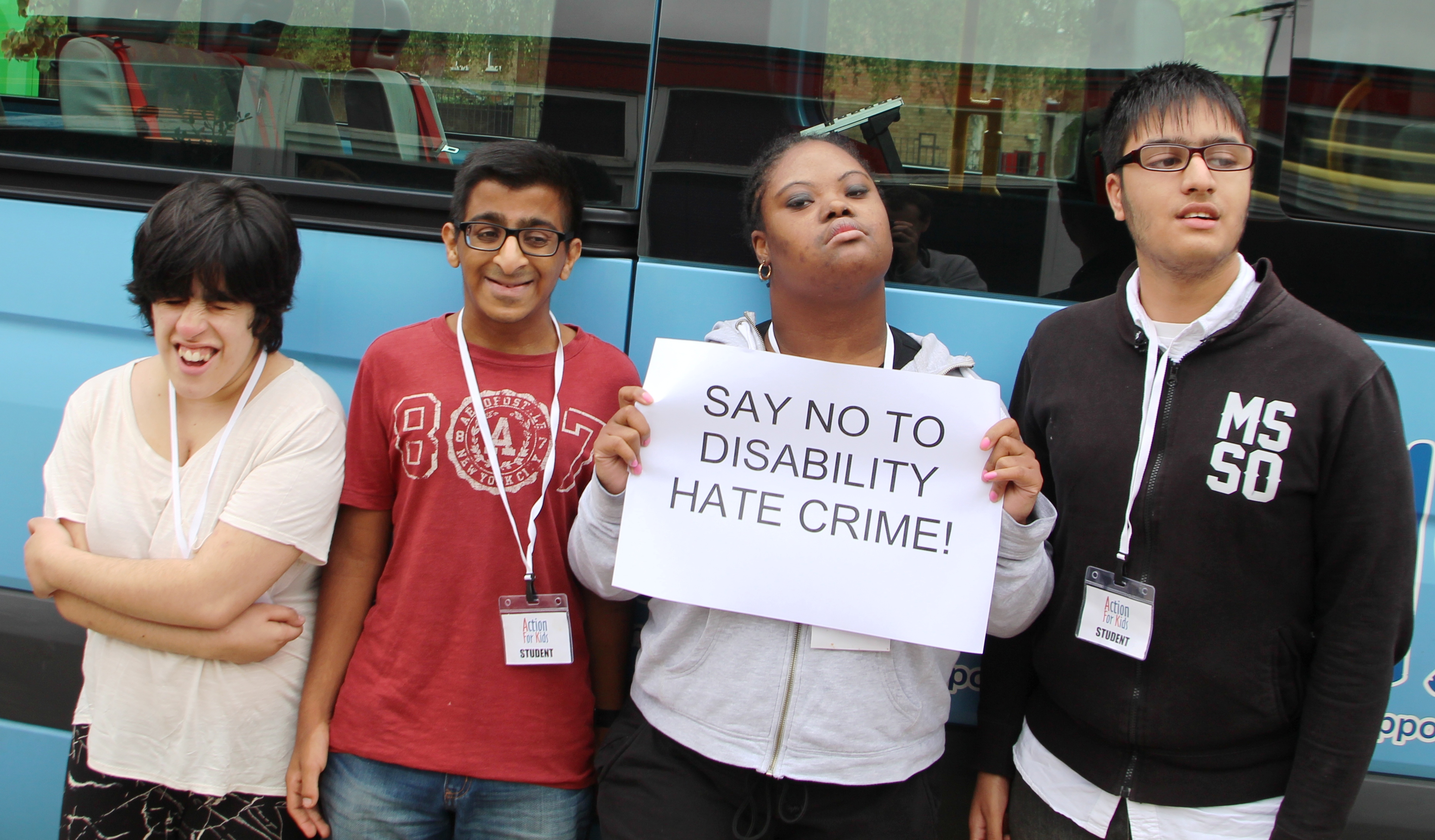 Four young people with learning disabilities, one holding a sign saying "no to disability hate crime"