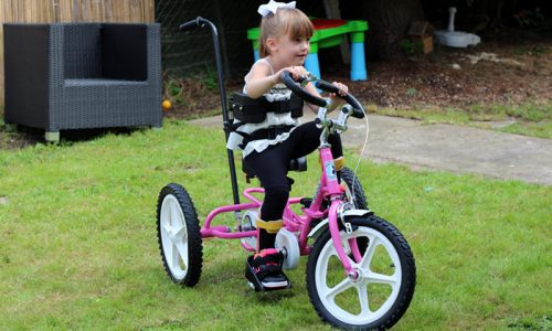 Young girl on a pink adapted trike in the garden