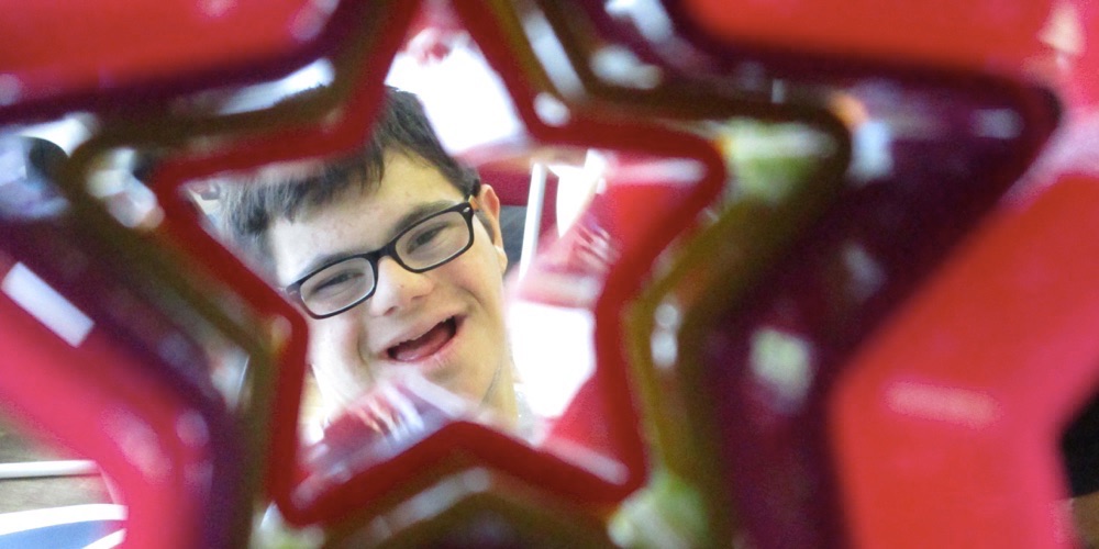 young boy with down syndrome smiling at camera through a star shaped cookie cutter