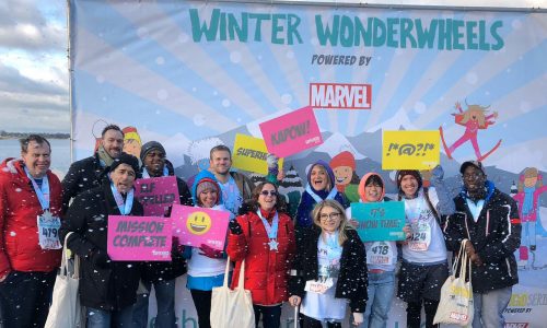a large group of people cheering and smiling in front of a winter background after finishing a marathon