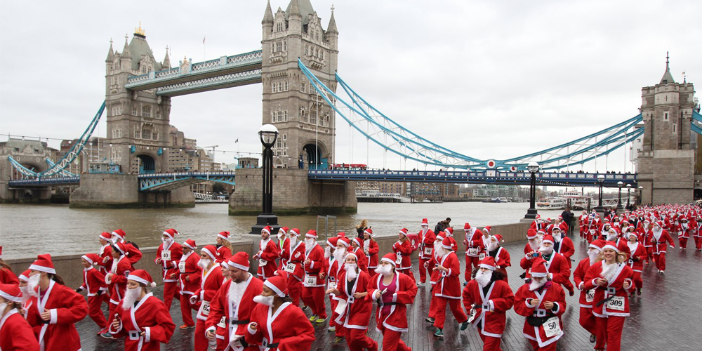 Crowd of runners in santa suits running with Tower Bridge in the background