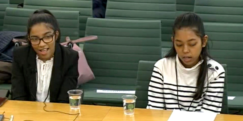 Two young women sitting at a table speaking to a conference room