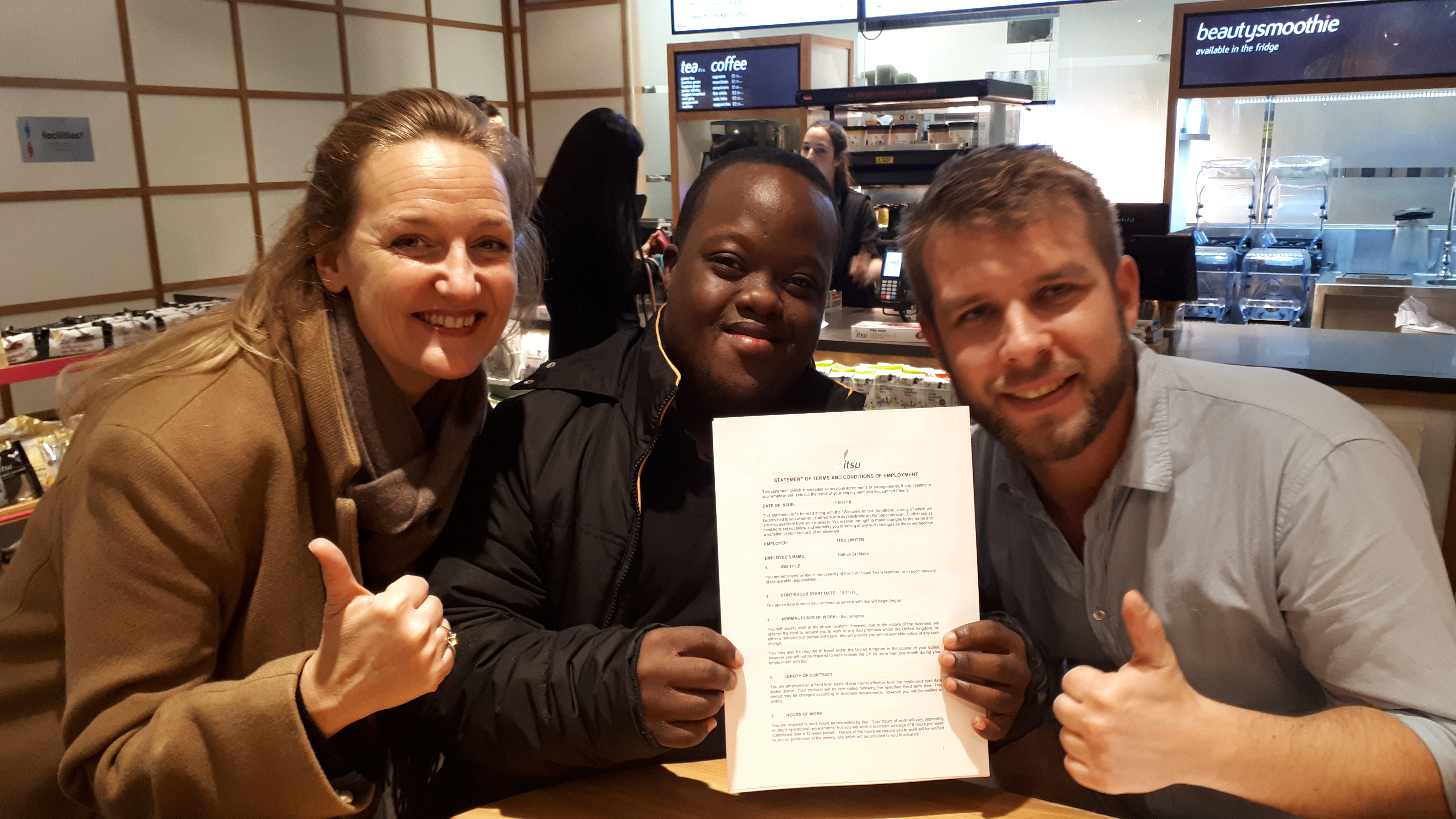 A young man with Down Syndrome with his managers, holding his work contract in an Itsu sushi resturant