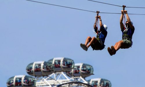 Two people on a zipwire with the London Eye in the background