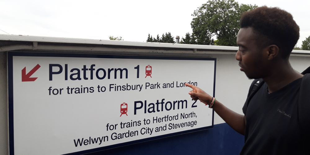 Young man with learning disabilities points to a sign in a train station as he decides his route