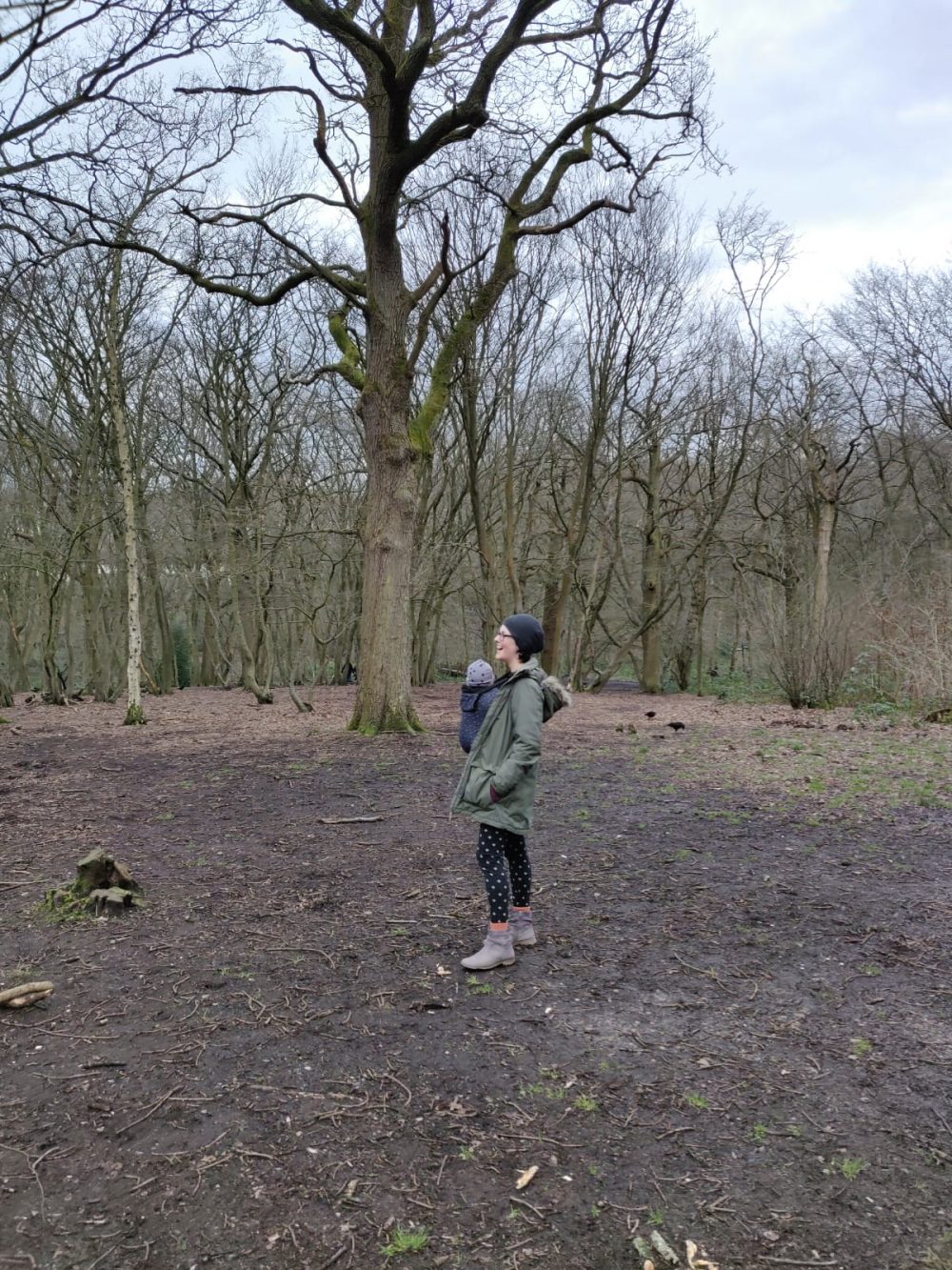 Jade standing in the wintry woods, with baby Ruth in a baby carrier