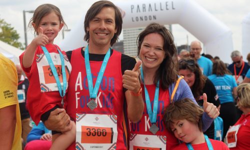 Family wearing red AFK vests and medals at Parallel London finish line
