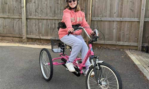 smiling girl riding pink trike wearing matching pink jumper