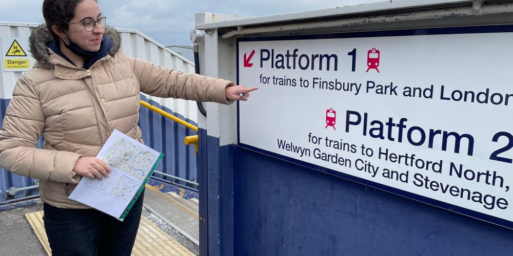Girl outdoors points to train platform signage