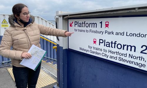 Girl outdoors points to train platform signage