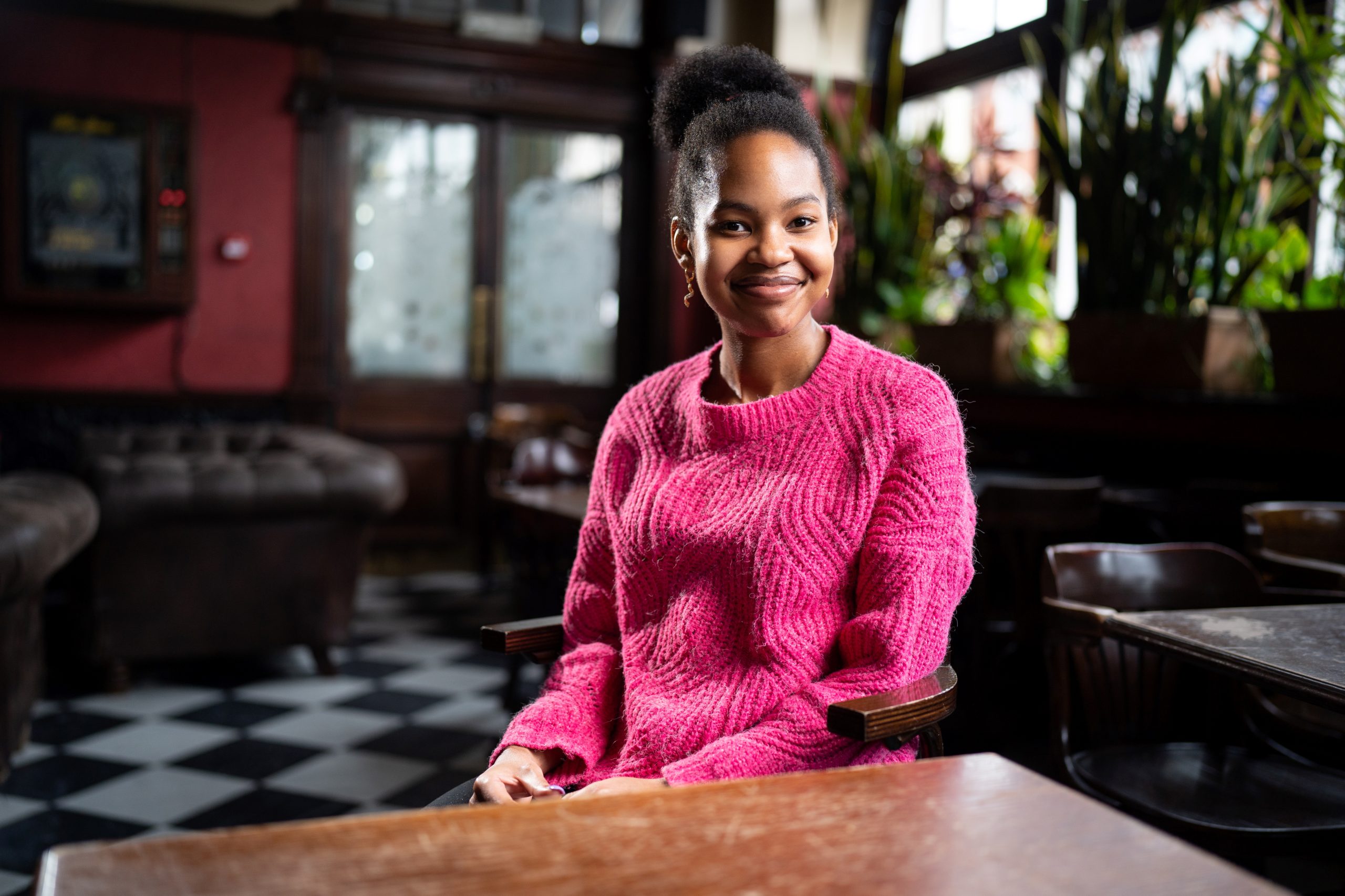 girl in pink jumper smiling at a table