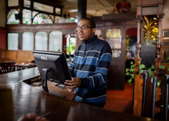 man behind a till at a bar in pub