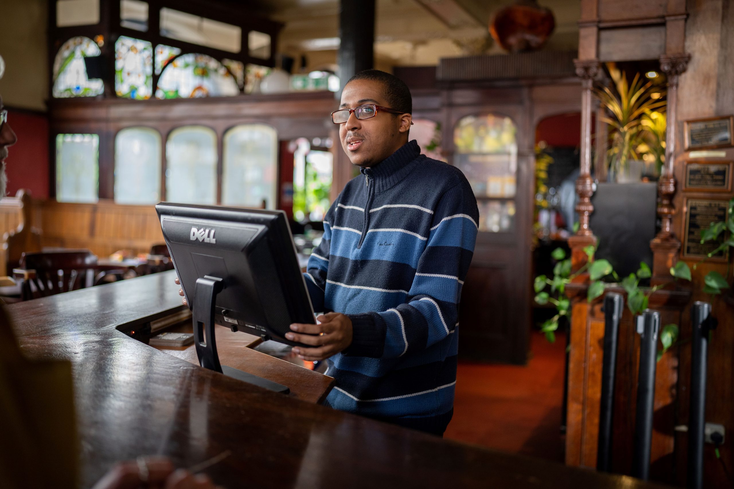 man behind a till at a bar in pub