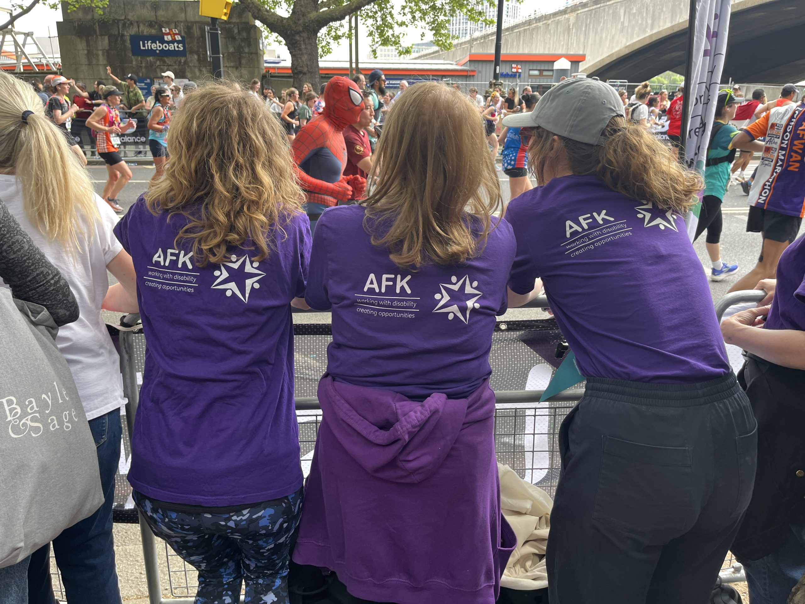 Three marathon spectators facing the london marathon with purple AFK t-shirts