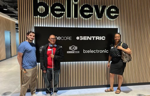 three people stood in front of a large 'believe' logo smiling