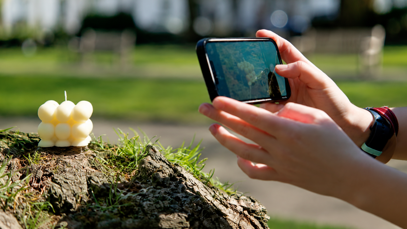 A young person photographs a handmade cream bubble candle outdoors for their small business.