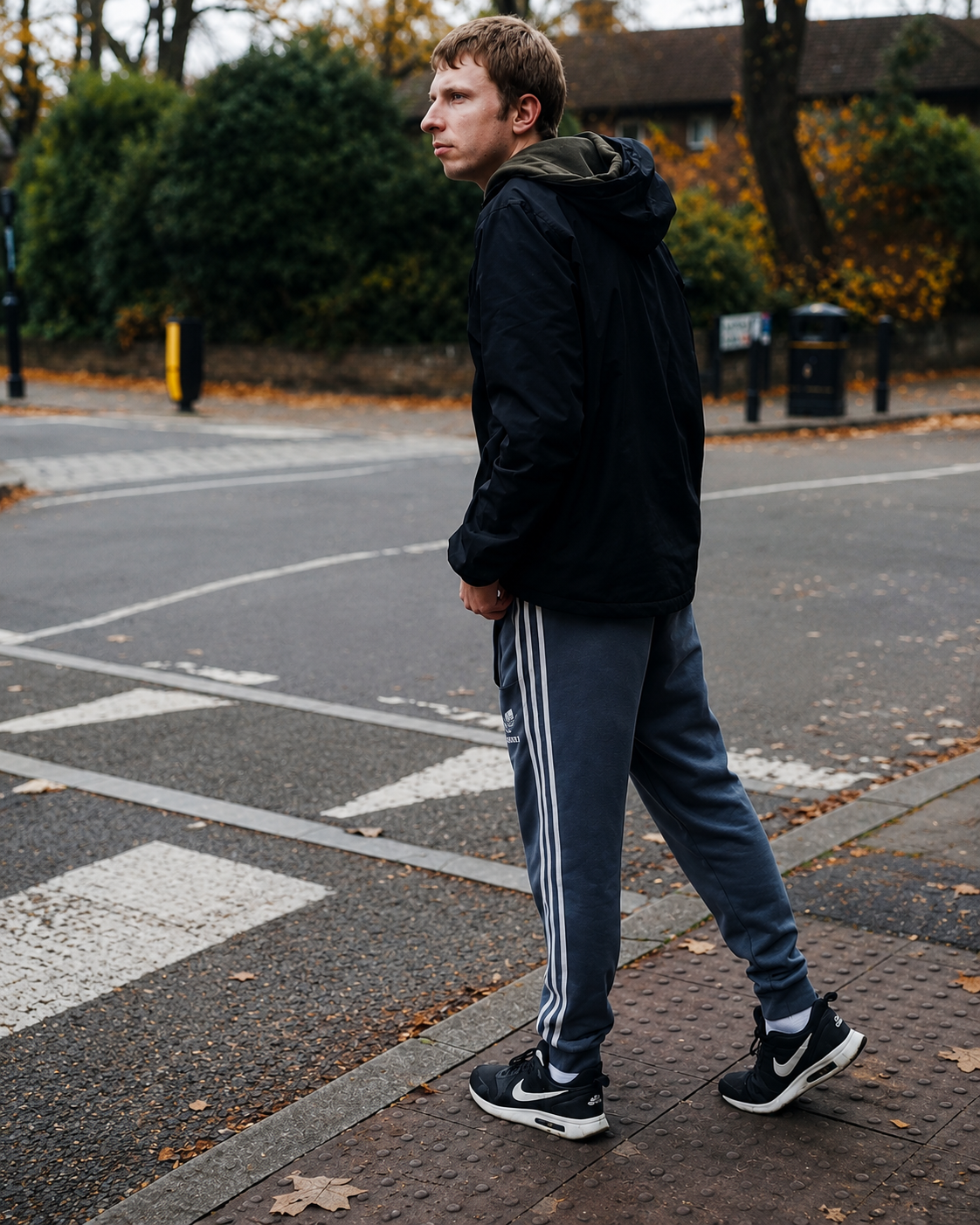 A young man stands at a pedestrian crossing, looking across the road before crossing.